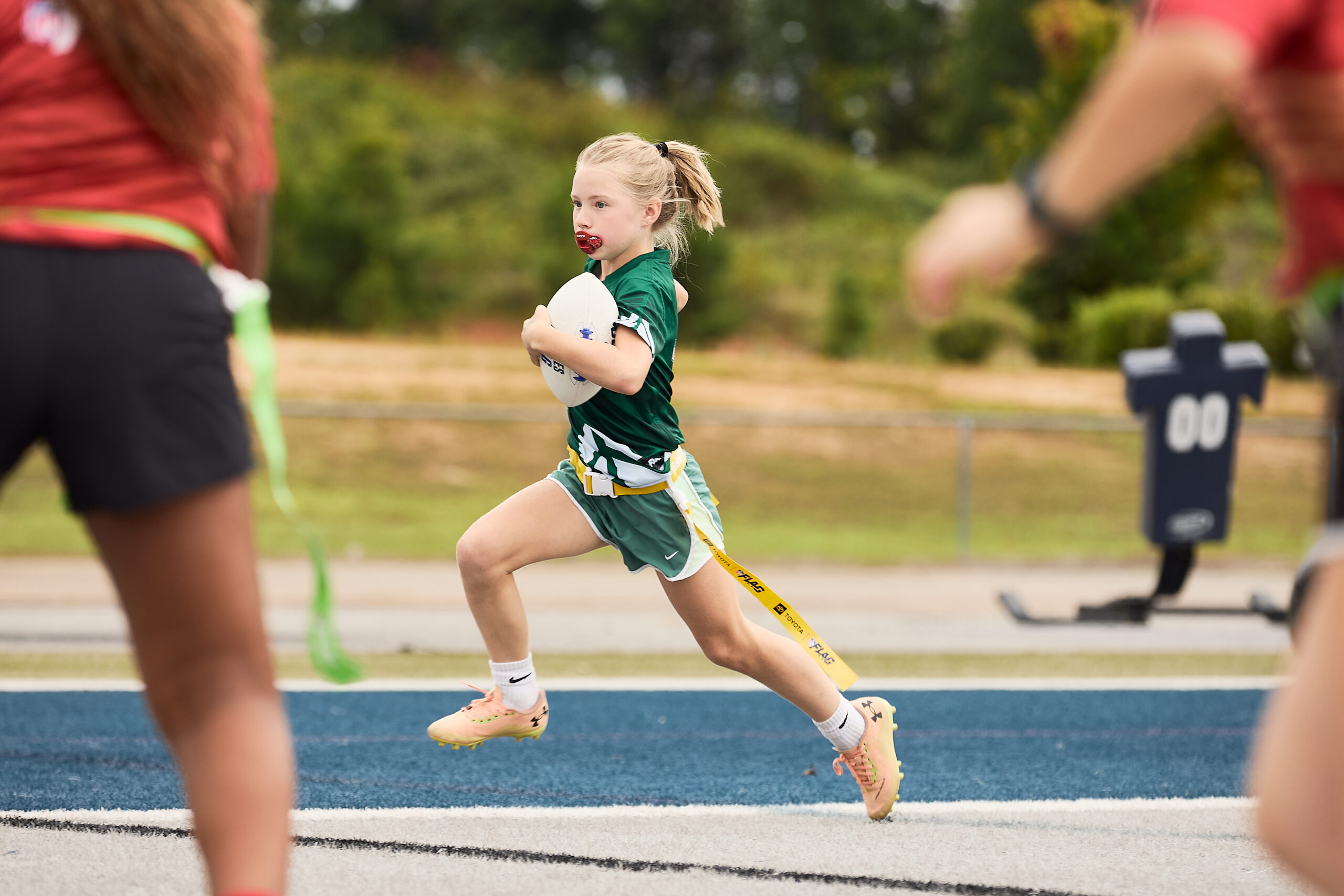 Girl sprinting down the field holding a flag football during a Girl Power Carolinas game.